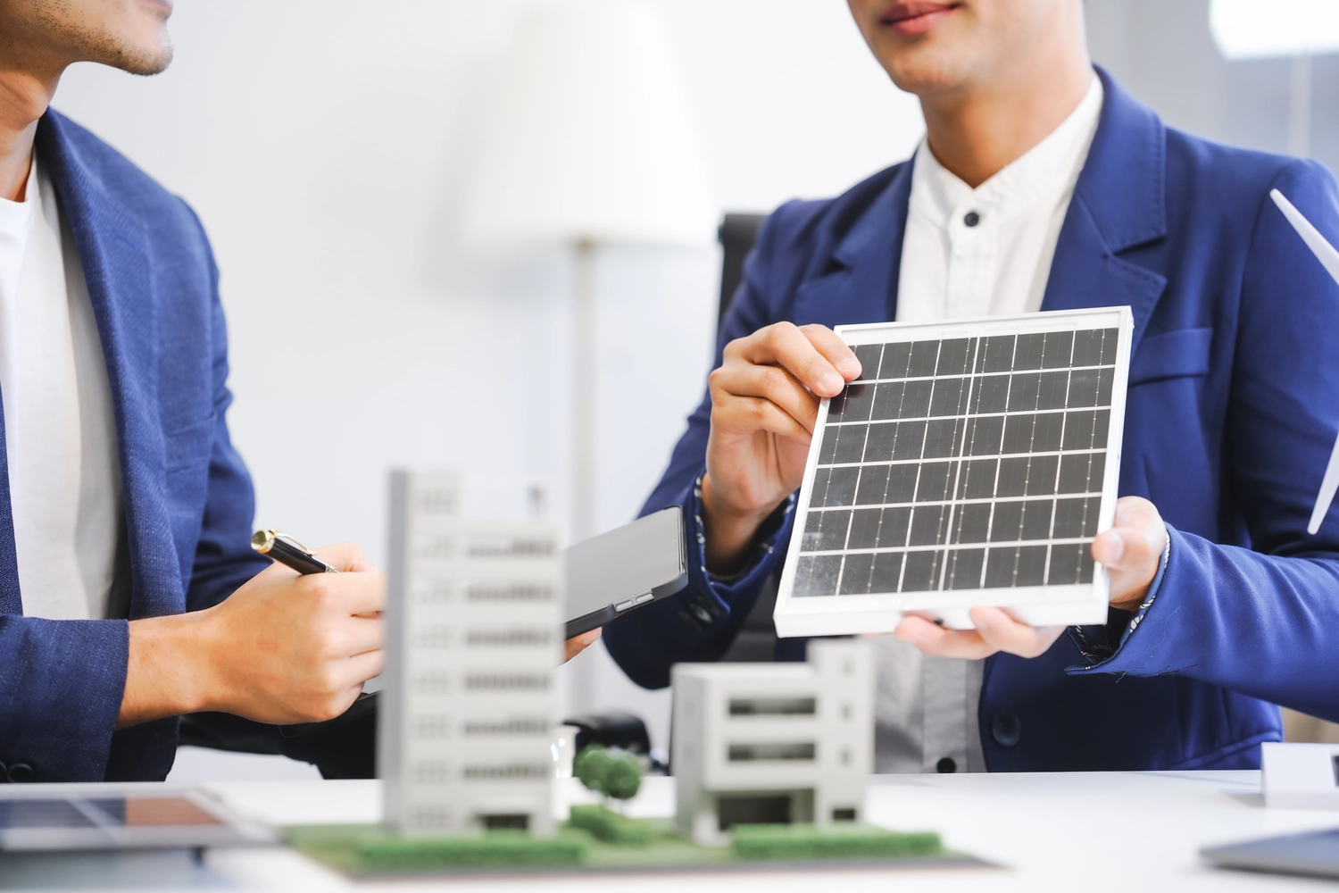 Deltatherm Energieberatung GmbH - Zwei asiatische Geschäftsleute treffen sich mit Windkraftingenieuren, um über Lösungen im Bereich erneuerbarer Energien zu diskutieren.